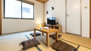 A traditional Japanese room with tatami flooring, a low wooden table, cushions, a television, and a sliding door. - Urban Stay Shinagawa (Tokyo)