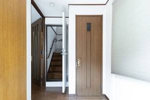 A hallway with a wooden door, a staircase, and a window with blinds. - Urban Stay Shinagawa (Tokyo)