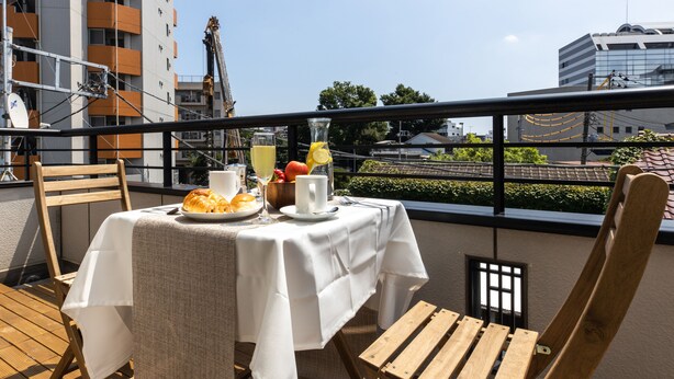 A balcony with a table set for breakfast, including croissants, fruit, and beverages. - Urban Stay Shinagawa (Tokyo)