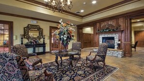 Un hall d’entrée spacieux, agrémenté d’un grand lustre, de fauteuils richement décorés, d’une table centrale ornée d’un arrangement floral et d’une cheminée.
