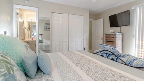 Une chambre à coucher comprenant un lit, deux portes, une commode, un téléviseur et un miroir.