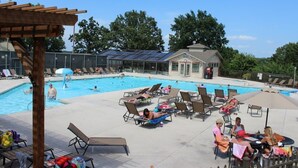 Un espace piscine comprenant des chaises longues, un coin salon abrité et un bâtiment doté d’un toit recouvert de panneaux solaires.