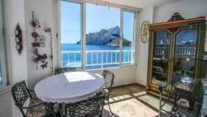 A room with a dining table, chairs, a ceiling fan, a large window with a view of the sea, and a glass cabinet with decorative items. - Angel - sea view apartment in Calpe (Calpe)