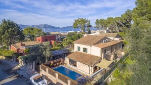 A coastal villa with a swimming pool, terraced roofs, and a view of the sea and mountains.