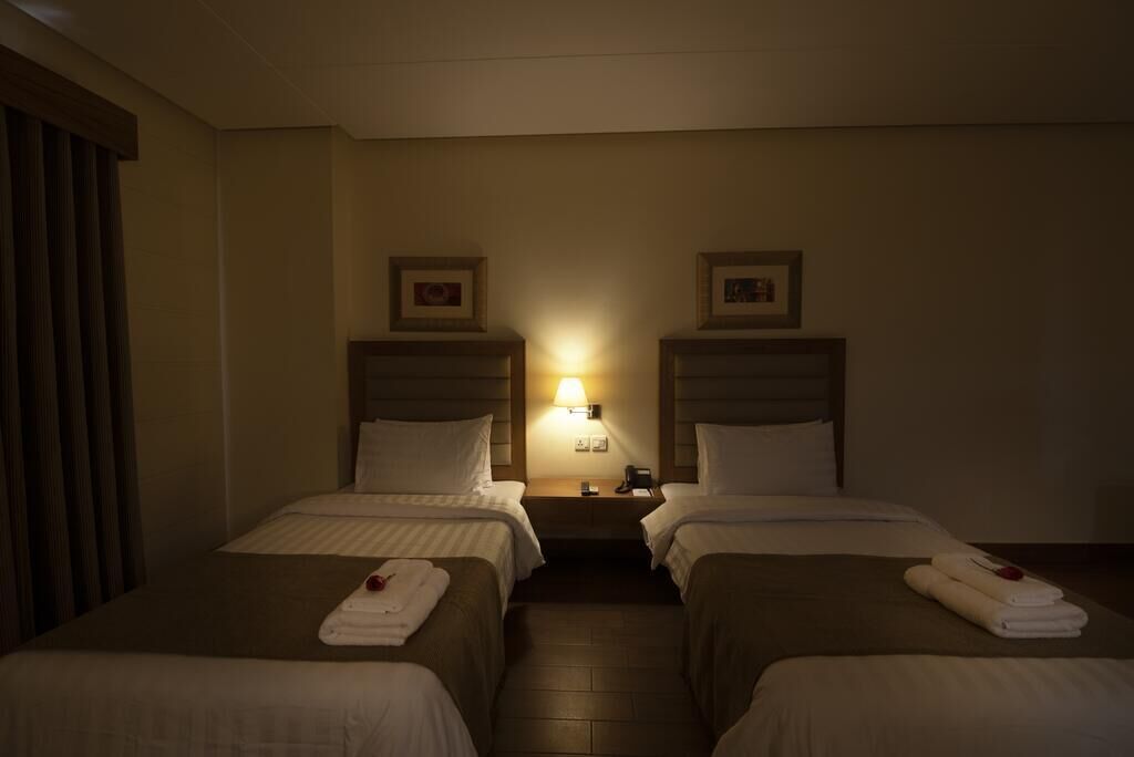 A hotel room with two beds, a nightstand with a lamp, and a window with curtains.