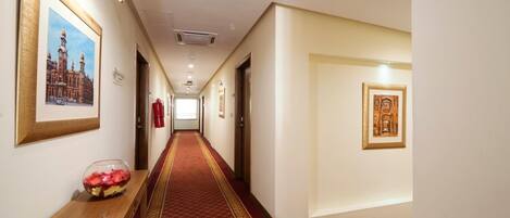 A hotel hallway with a red carpet, framed pictures on the walls, and a wooden bench with a decorative bowl.