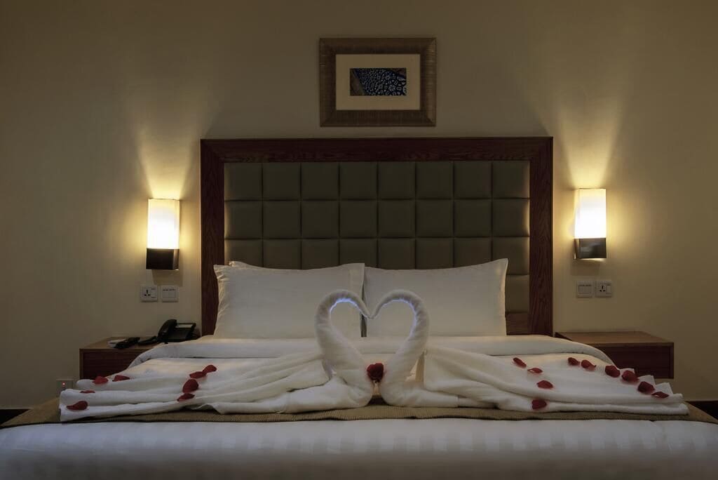 A hotel room with a bed, two bedside lamps, a framed picture on the wall, and a telephone on the nightstand.