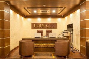A reception desk with two laptops, a sign reading "Hotel One", and two brown chairs. - Hotel One Tariq Road Multan (Multan)