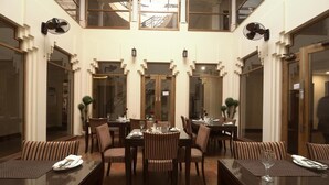 A dining area with multiple tables and chairs, large windows, and ceiling fans. - Hotel One Tariq Road Multan (Multan)