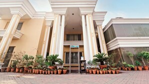 A hotel entrance with a central doorway flanked by columns, surrounded by potted plants. - Hotel One Tariq Road Multan (Multan)