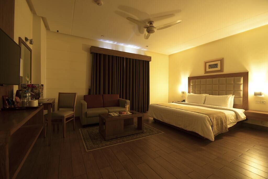 Una habitación de hotel con cama, sofá, mesa de centro, televisión y ventilador de techo.