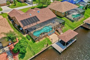 A residential property with a swimming pool, solar panels, and a dock over a water body. - Blue Haven Large Waterfront Pool Home | Boat Dock | Canal | Water Views | Pool Bar | WIFI | Fishing (Palm Coast)