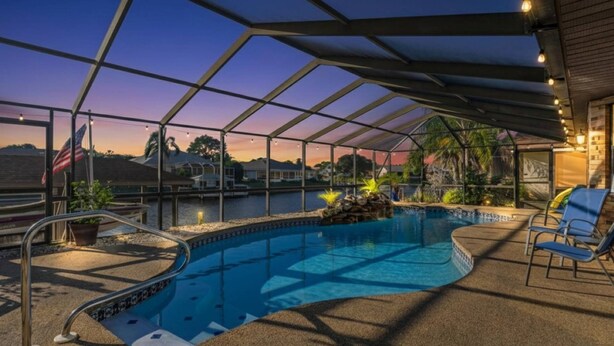 An indoor swimming pool with a glass ceiling, surrounded by lounge chairs and a view of the sunset.
