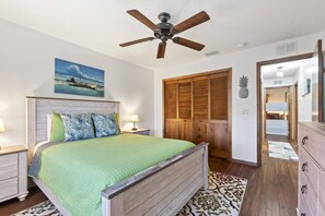 A bedroom with a wooden bed, a ceiling fan, a painting of a boat, a wooden wardrobe, and a mirror. - Blue Haven Large Waterfront Pool Home | Boat Dock | Canal | Water Views | Pool Bar | WIFI | Fishing (Palm Coast)