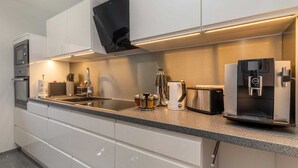 Une cuisine moderne avec des armoires blanches, un four encastré, une machine à café, un grille-pain et un réfrigérateur.