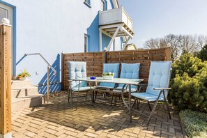 A patio with a table and four chairs, a wooden fence, and a blue building with a balcony.