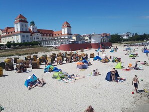A beach with beach chairs and umbrellas, a large building with towers, and a sandy shore.