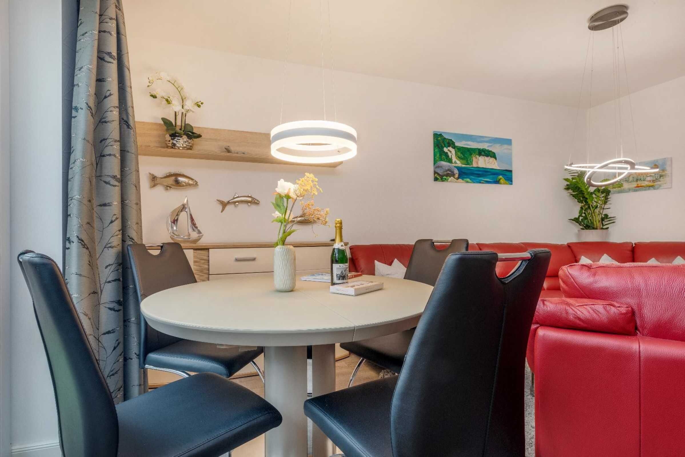 A dining area with a round table, black chairs, a red sofa, decorative fish wall art, a painting, and a hanging light fixture.