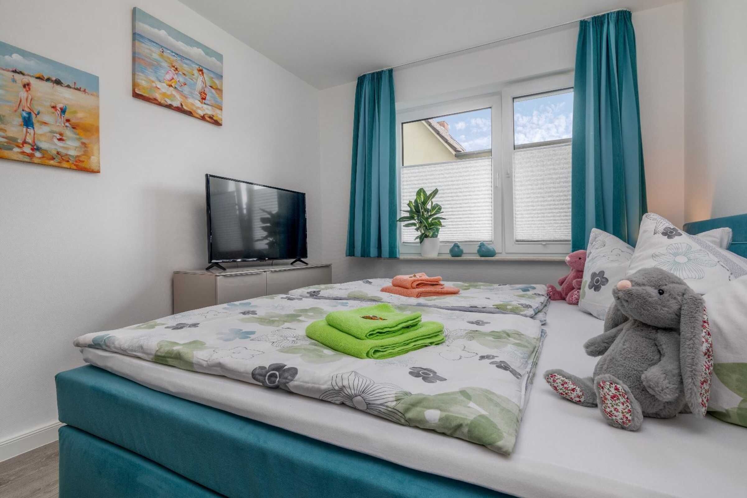 A bedroom with a bed, a TV, a window with curtains, and a painting on the wall.