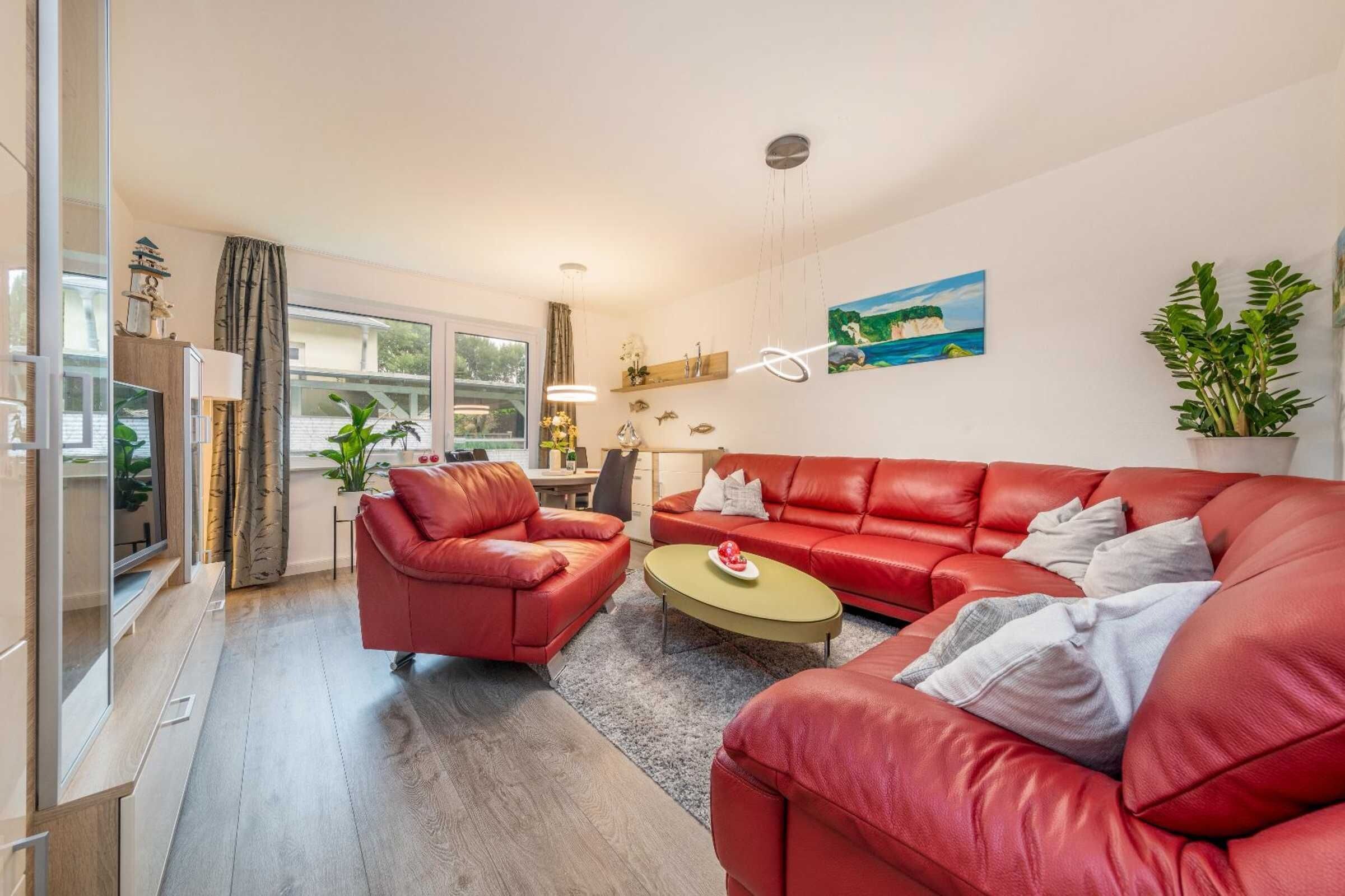 A modern living room with a red leather sofa, a coffee table, and a painting on the wall.