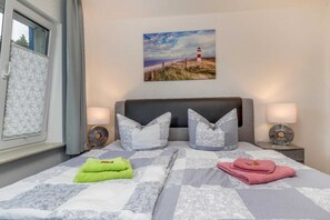 A neatly made bed with patterned bedding, two bedside lamps, and a framed picture of a lighthouse on the wall.