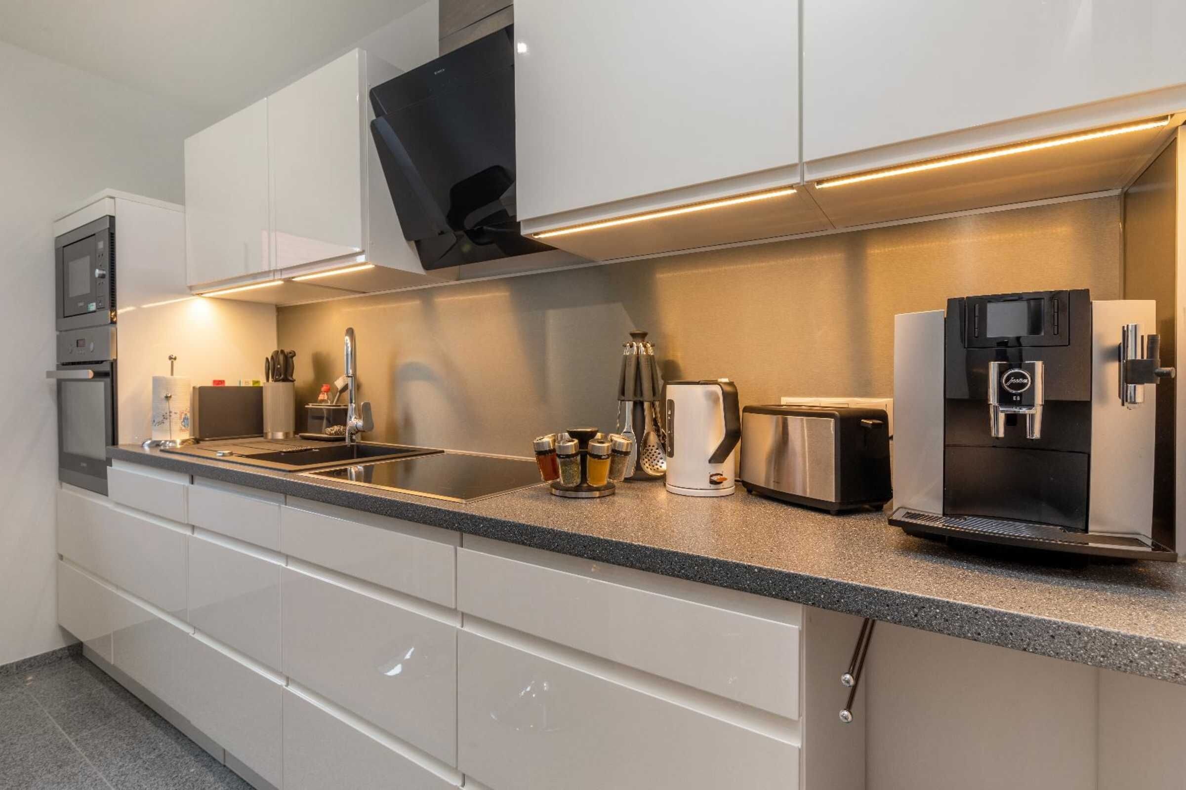 A modern kitchen with white cabinets, a built-in oven, a coffee maker, a toaster, and a refrigerator.