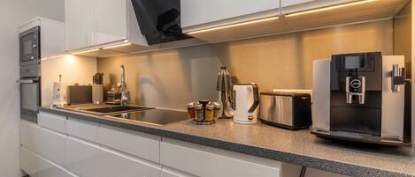 A modern kitchen with white cabinets, a built-in oven, a coffee maker, a toaster, and a refrigerator.