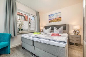 A bedroom with a bed, a window with curtains, a nightstand, a lamp, and a painting on the wall.