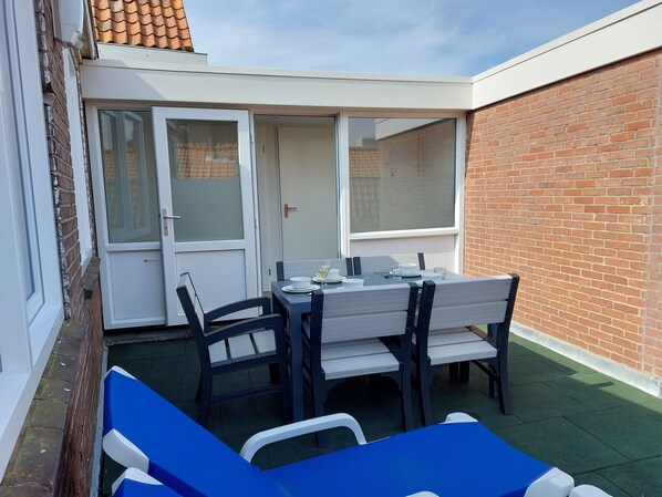 A patio with a table set for two, surrounded by chairs, and a blue lounge chair. - Apartment 105.2, 200 meters from the beach (Westkapelle)
