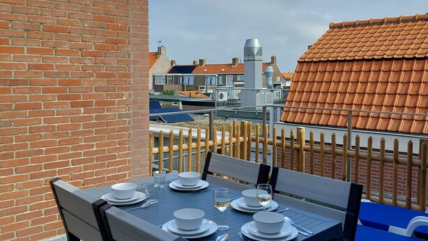 A rooftop terrace with a table set for dining, overlooking a cityscape with traditional buildings.