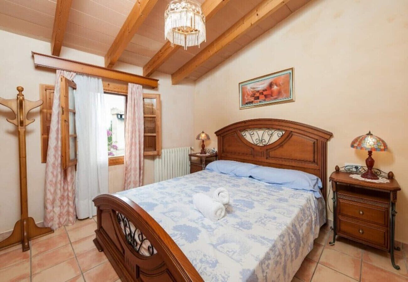 A bedroom with a wooden bed, a nightstand, a chandelier, and a window with curtains.