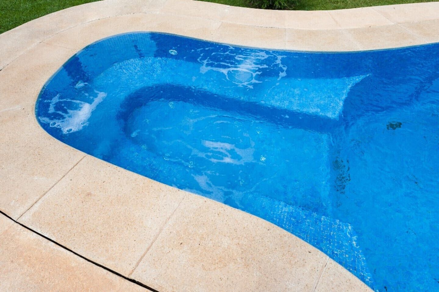 Ein Pool mit geschwungener Kante und einer hell gefliesten Terrasse darum.