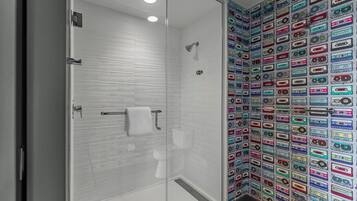 A bathroom with a glass shower enclosure, a white tiled wall, and a wall covered with colorful cassette tapes.