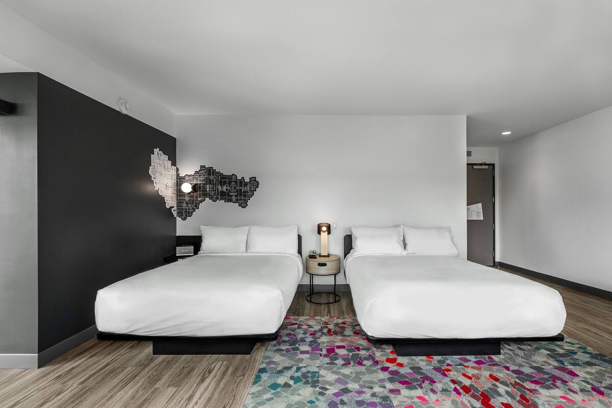 A modern hotel room with two single beds, a patterned rug, and a wall art piece.
