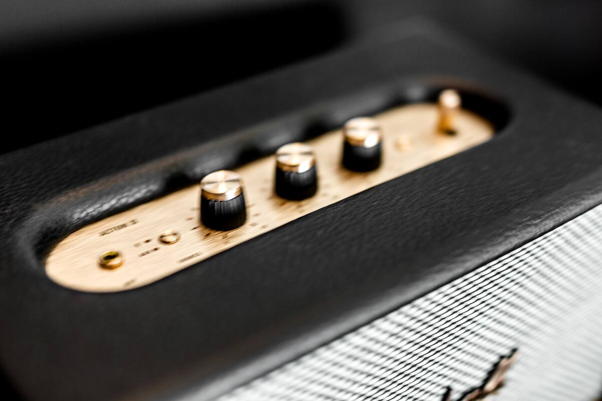 A close-up of a black speaker with a wooden panel and four knobs.