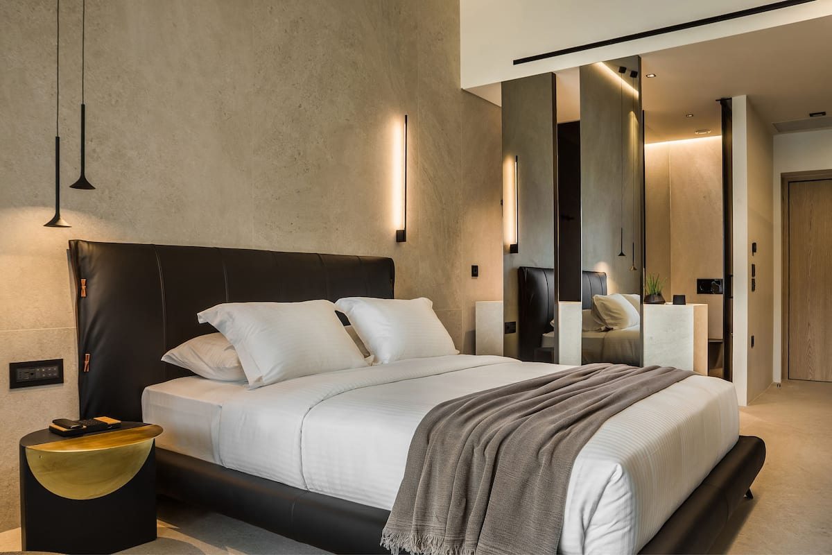 A modern bedroom with a large bed, bedside tables, a mirror, and a wall-mounted light fixture.