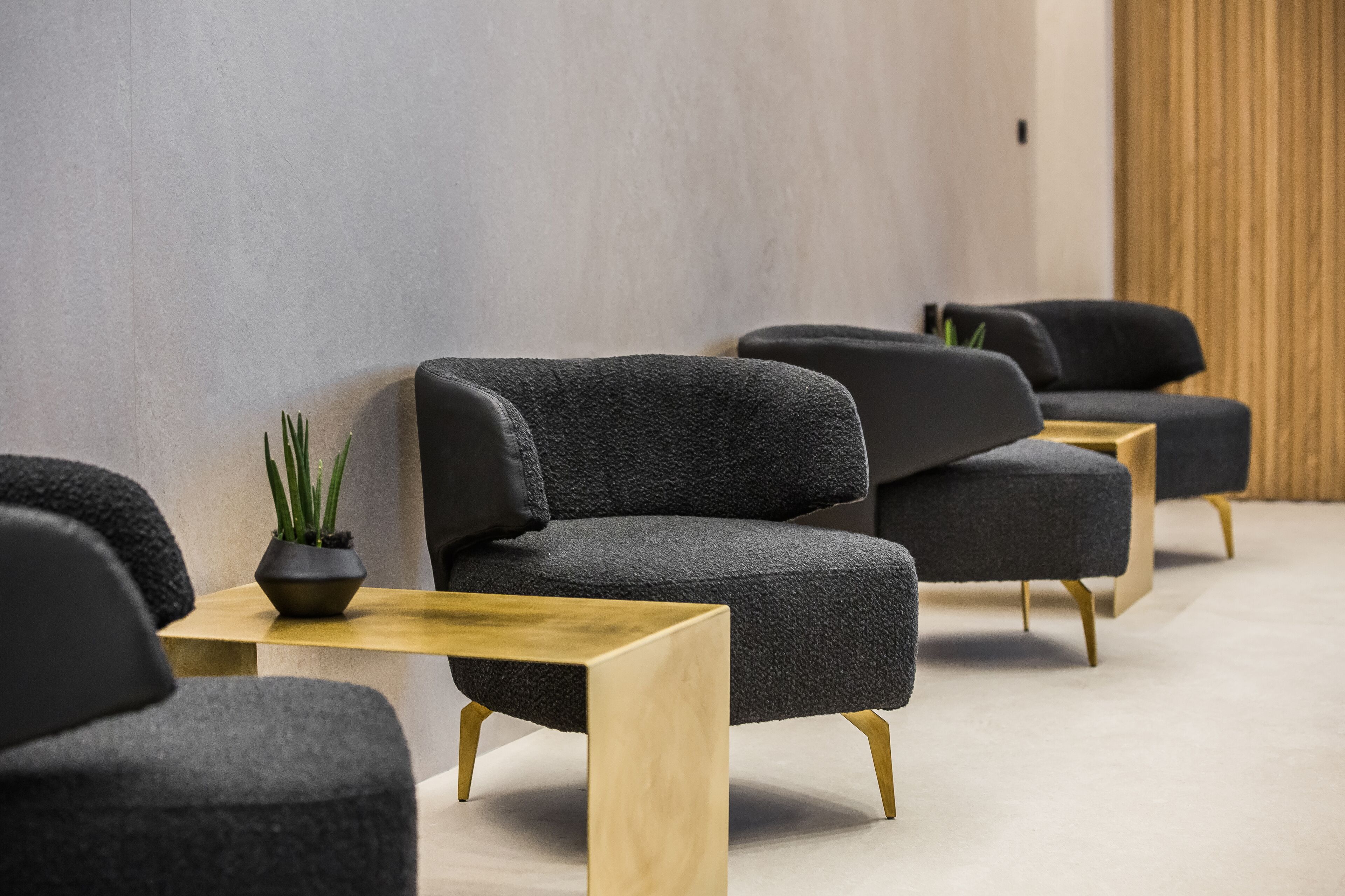 Ein modernes Interieur mit grau gepolsterten Sesseln, Holztischen und einem Topfpflanzen.