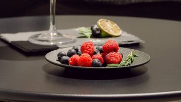 Um copo de martini com uma bebida cítrica, um prato de framboesas e mirtilos, e uma fatia de limão sobre uma mesa.