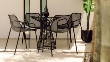 A modern outdoor dining area with a round table and chairs, a potted plant, and a view of a building through a window.