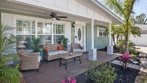 Una veranda coperta con mobili in vimini, una ventola a soffitto e vista sulla casa.