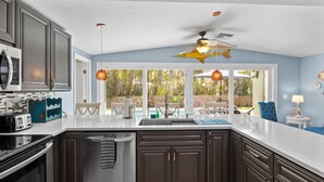 Una cucina moderna con mobili scuri, una grande isola e vista su un giardino con piscina.