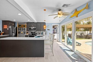 A modern kitchen with a large island, dark cabinets, and a view of an outdoor pool area. - Island Getaway: Tropical Oasis Backyard, Pool, Dog Friendly, 1.5 blocks to Beach by Anna Maria Life (Holmes Beach)