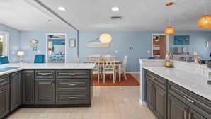 Una cucina moderna con mobili scuri, un piano di lavoro bianco e un'area pranzo con tavolo e sedie.