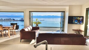 A modern living room with a large leather sofa, a dining area with a table and chairs, and a TV mounted on the wall.