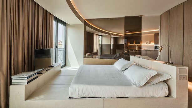 A modern hotel room with a large bed, a TV, and a seating area with books. - RESIDENZA II LUXURY APARTMENT (Cattolica)