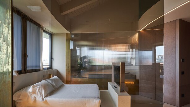 Ein modernes Schlafzimmer mit einem großen Bett, einer Glastrennwand und Blick auf die Stadt.