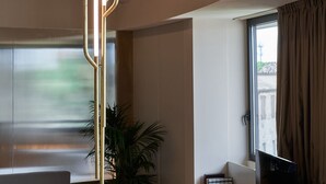 Ein modernes Wohnzimmer mit großem Fenster, einer Pflanze und einem Fernseher auf einem Standfuß.