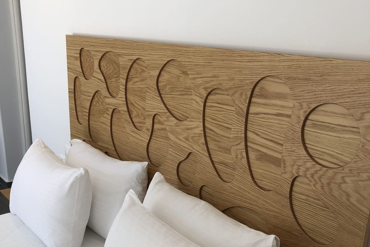 Een bed met een houten hoofdbord, versierd met een bladmotief, en versierd met meerdere witte kussens.