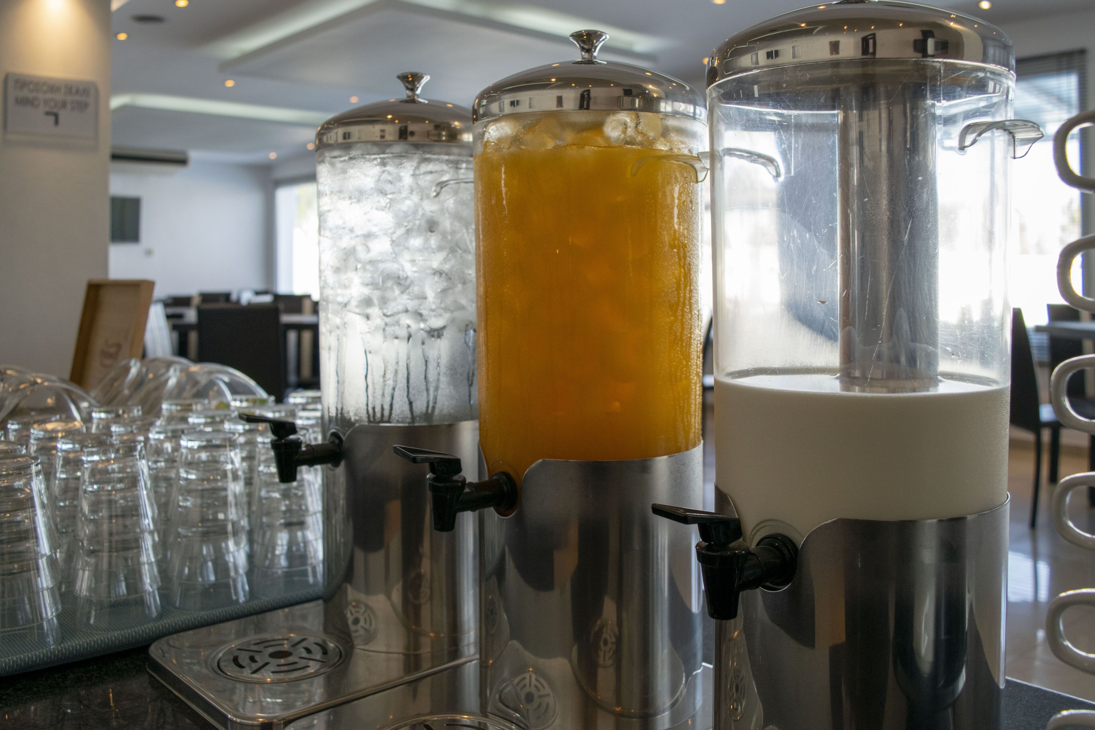 Trois distributeurs de boissons équipés de becs verseurs et de robinets, une rangée de verres vides et un panneau avec un logo.