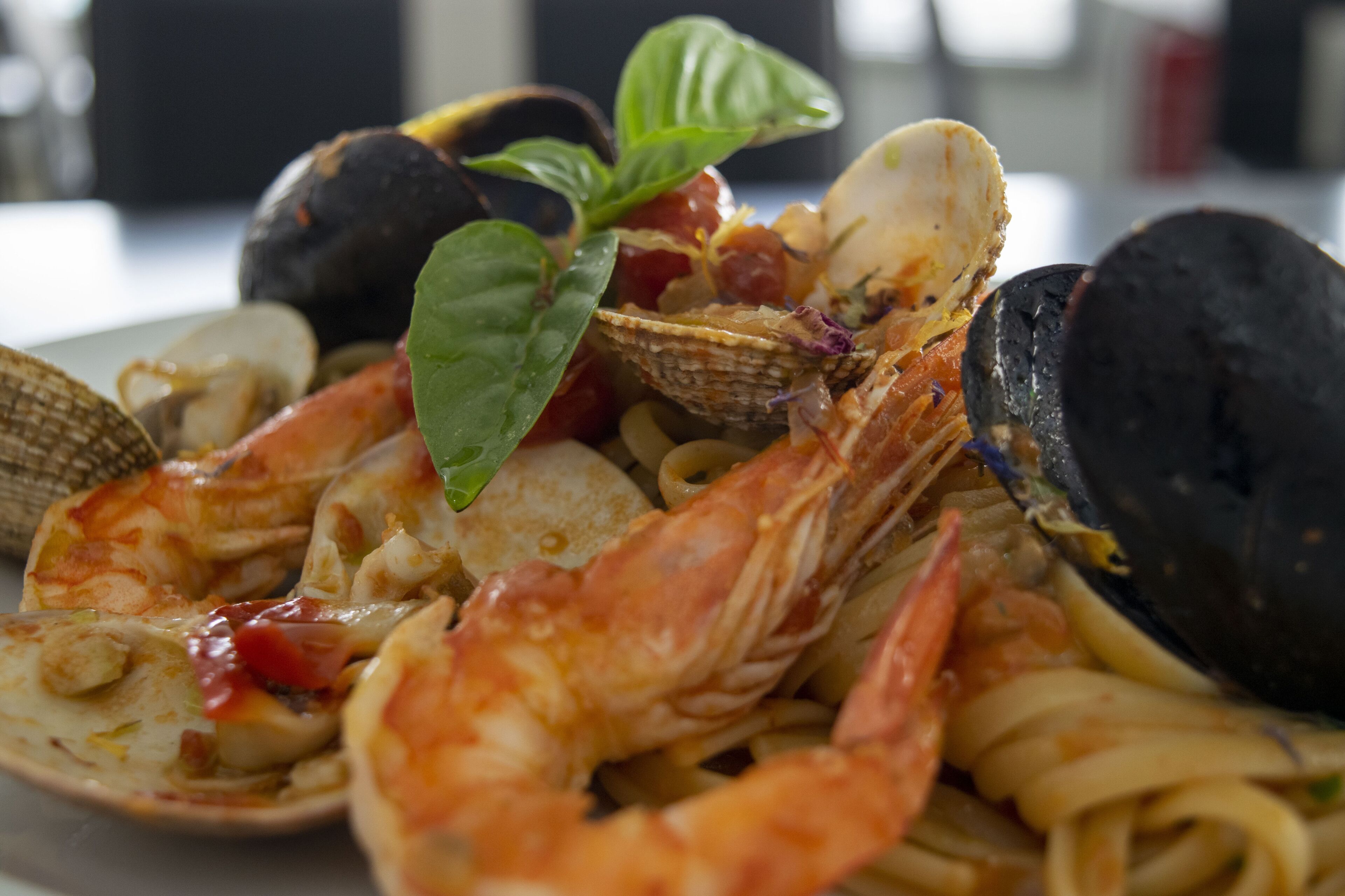 Ein Meeresfrüchte-Pasta-Gericht mit Garnelen, Muscheln, Venusmuscheln und Basilikum-Blatt-Garnitur.